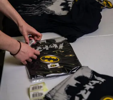 barcode label being stuck onto a packaged Batman printed t-shirt.
