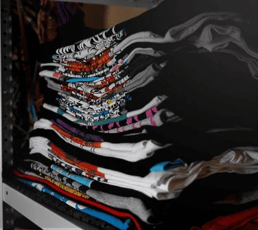A stack of screen printed black t-shirts, neatly folded on a retail shelf.