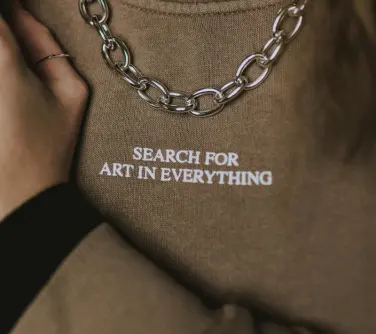 white that reads "search for art in everything"embroidery on a brown sweatshirt.
