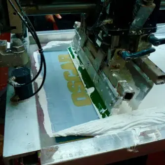 an automated screen printing machine pulling white ink across a mesh design.